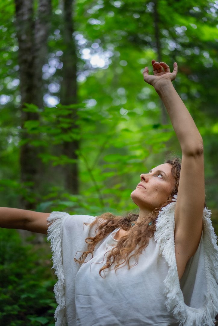 Robyn in the forest, one arm raised to the light