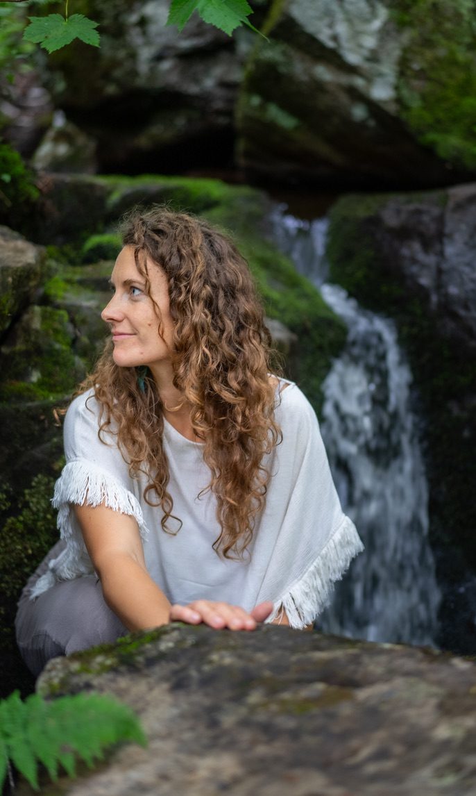 Robyn leaning against a mossy rock by a waterfall, smiling