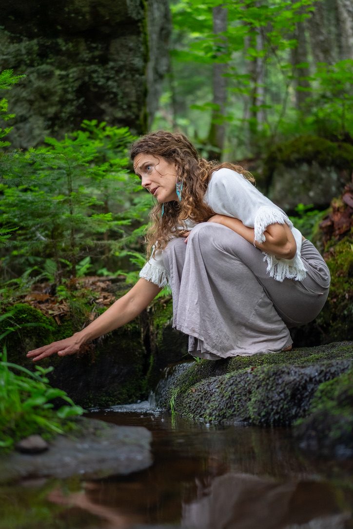Robyn crouched by a forest stream, her hand in the water